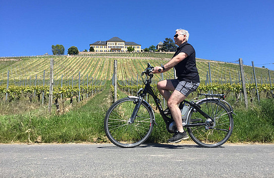 A white man e-biking past vineyards on a sunny day