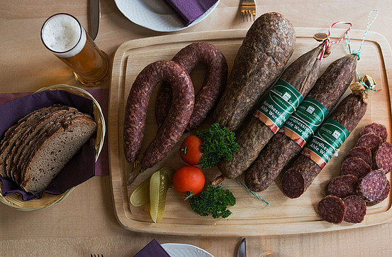 A wooden platter of whole Ahle Wurscht with a basket of bread alongside