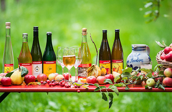 A row of bottles of apple wine and brandies next to a basket of apples